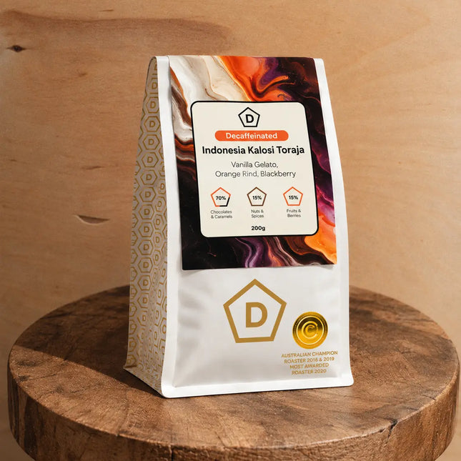 Danes Indonesia Kalosi Toraja decaf coffee bag displayed on a rustic wooden stool against a warm timber background.