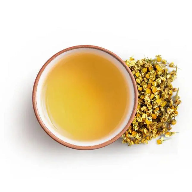 A cup of chamomile tea with dried chamomile flowers, showcasing the herbal tea by ORIGIN Teas in a cozy setting.